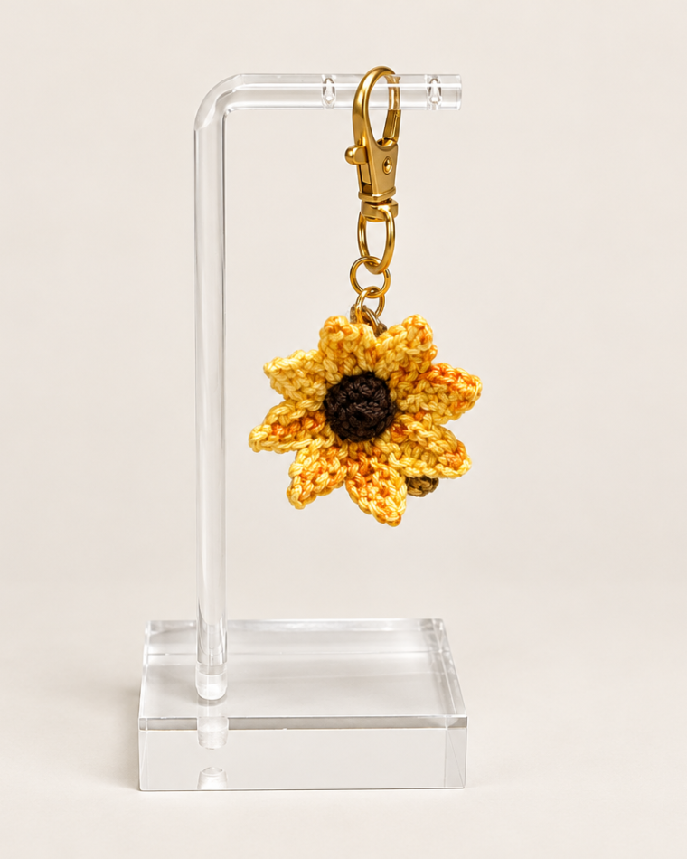 Yellow and golden sunflower badge charm with a dark center and gold-tone clasp on a clear display stand.