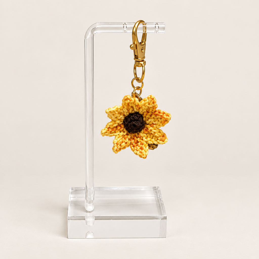 Yellow and golden sunflower badge charm with a dark center and gold-tone clasp on a clear display stand.